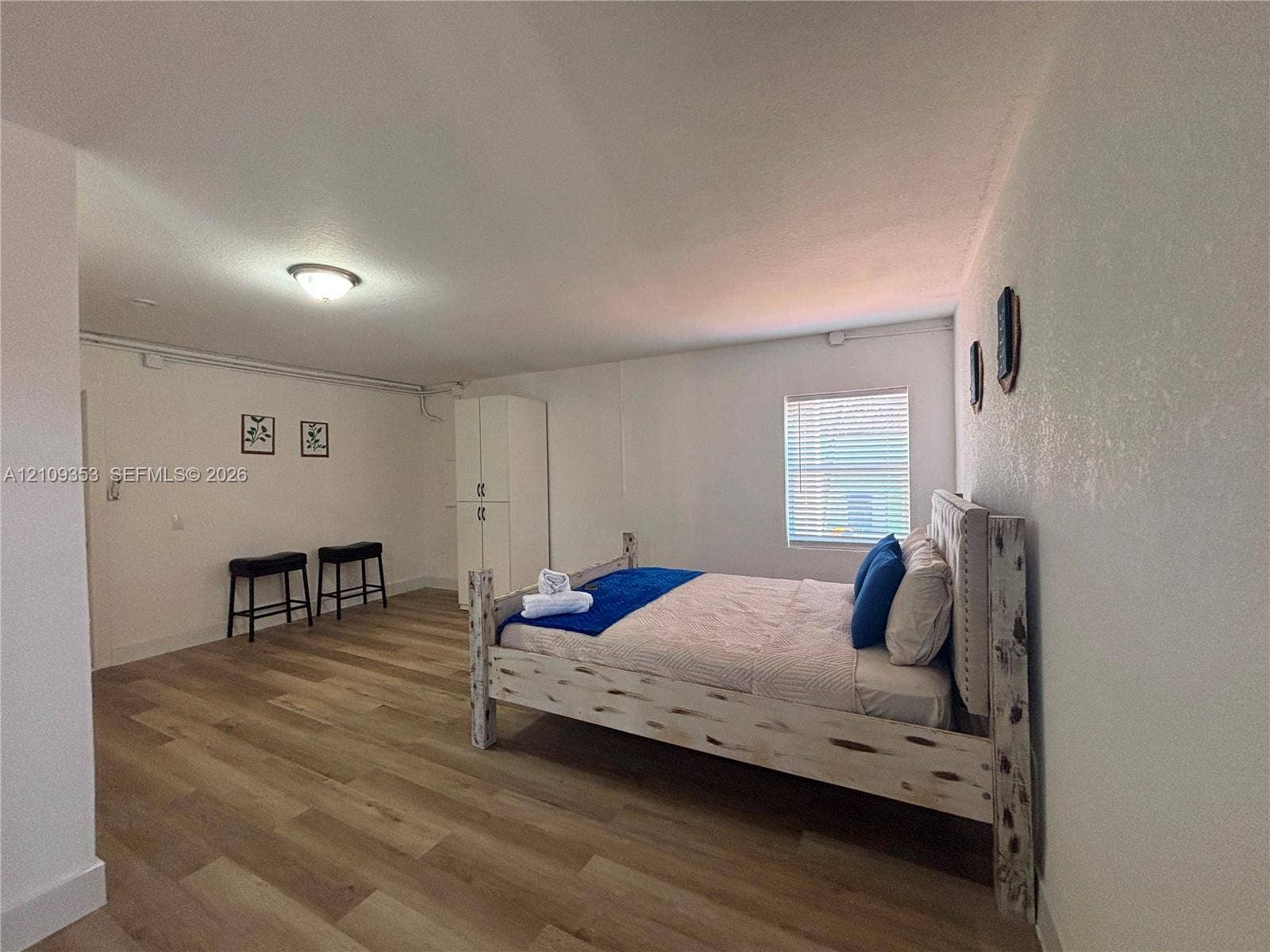 Wood-finish flooring, white-finish built-in cabinetry, and a window with horizontal blinds