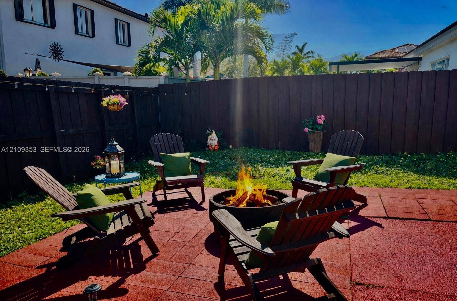 Rear patio featuring a fire pit, paved flooring, perimeter wood fencing, and mature palm trees