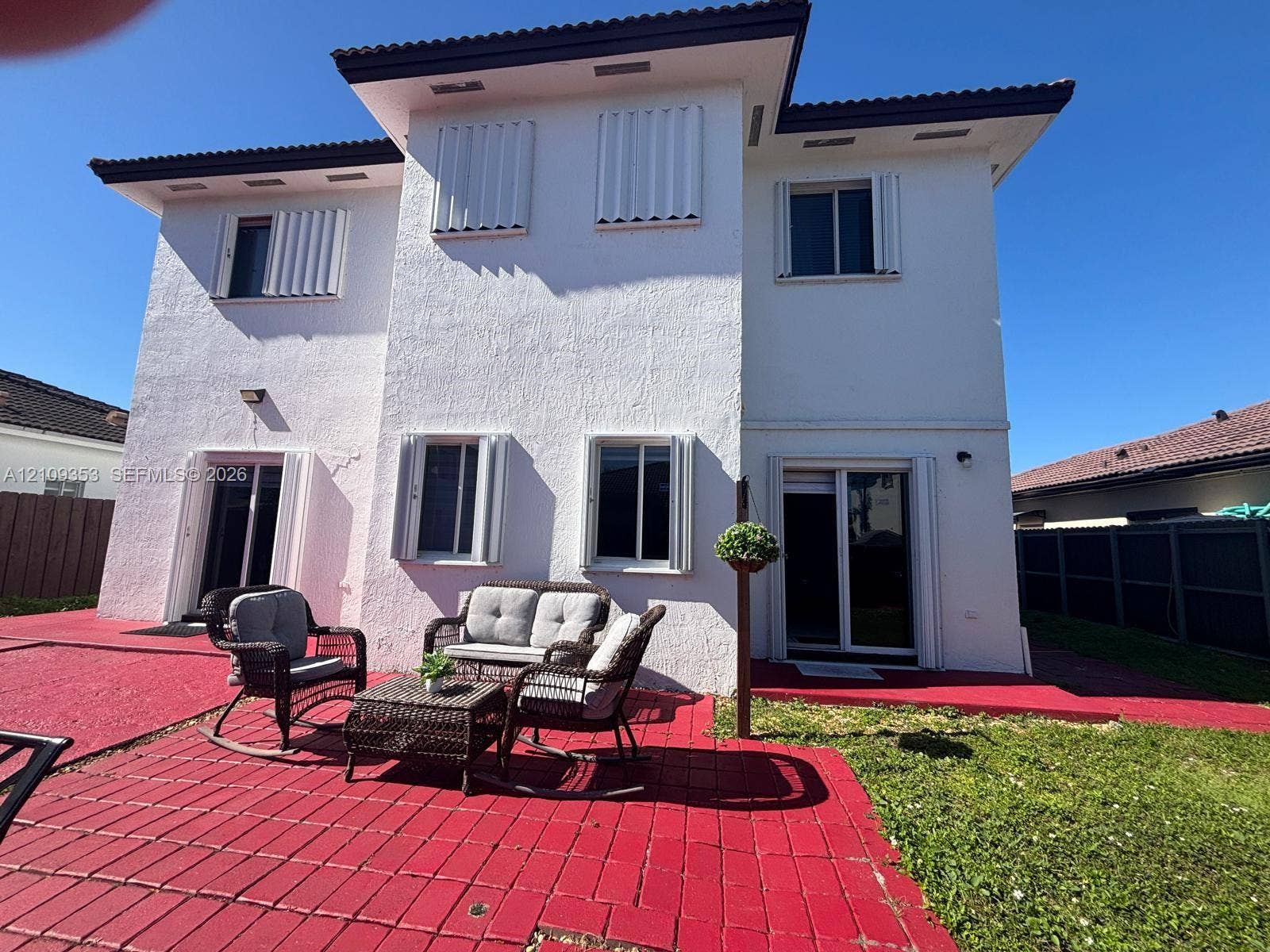 Two-story stucco exterior featuring a red paver patio, accordion storm shutters, and sliding glass door access
