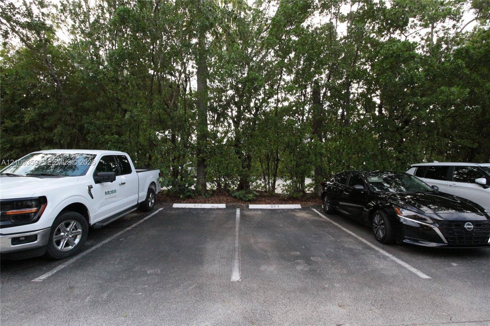 2426 SE 17th Causeway, #103A, Fort Lauderdale, FL 33316 Asphalt parking area featuring two designated spaces and a perimeter of mature trees