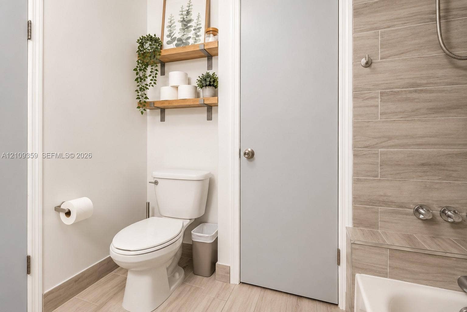 2426 SE 17th Causeway, #103A, Fort Lauderdale, FL 33316 Bathroom featuring wood-finish floor tiling, wall-mounted floating shelves with metal brackets, a two-piece toilet, and tile-surround tub area