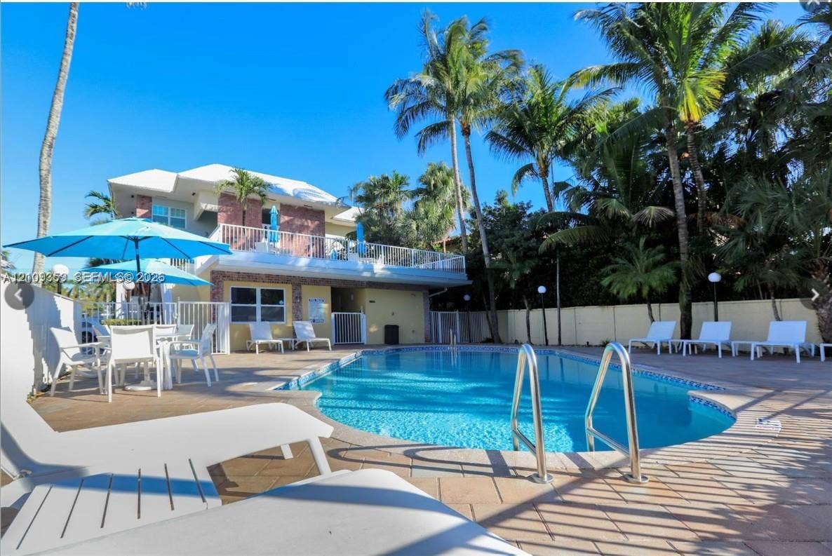 2426 SE 17th Causeway, #103A, Fort Lauderdale, FL 33316 In-ground swimming pool with metal ladder, expansive paver patio, second-story railed balcony, and mature palm trees