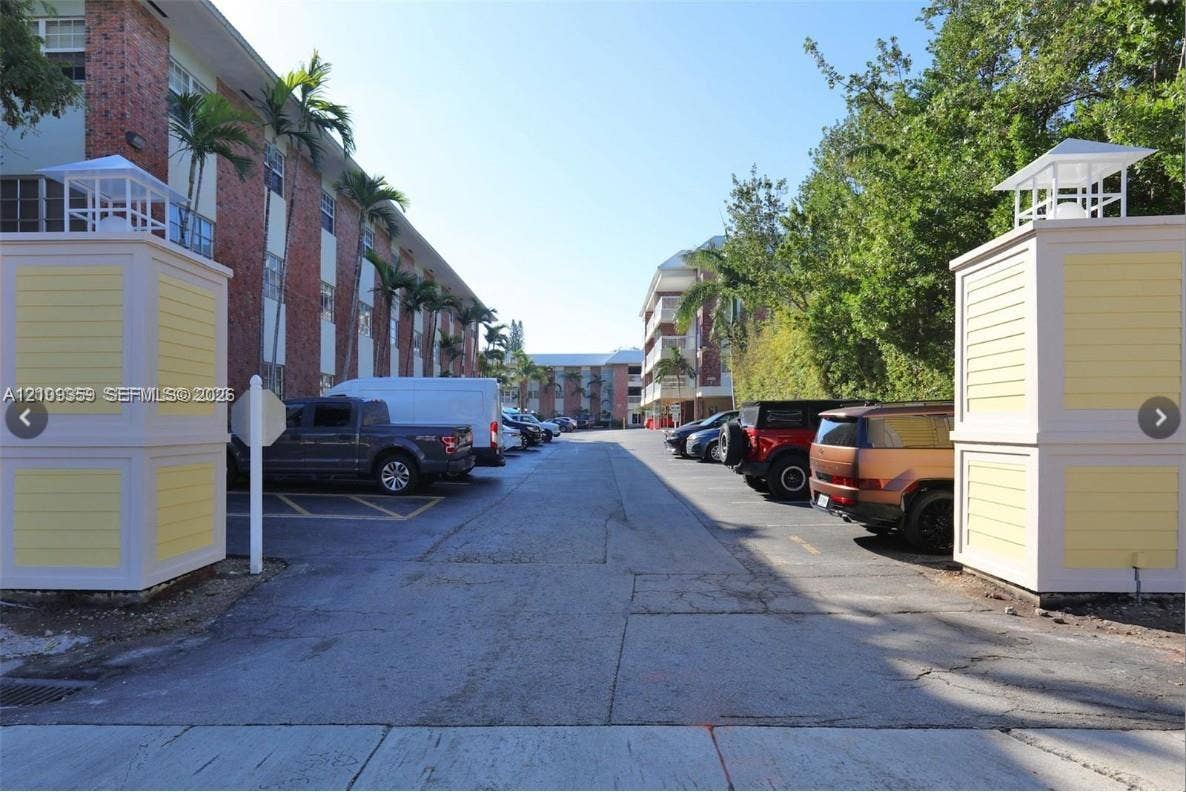 2426 SE 17th Causeway, #103A, Fort Lauderdale, FL 33316 Gated entrance featuring decorative columns with roof caps, paved surface parking area, and mature landscaping