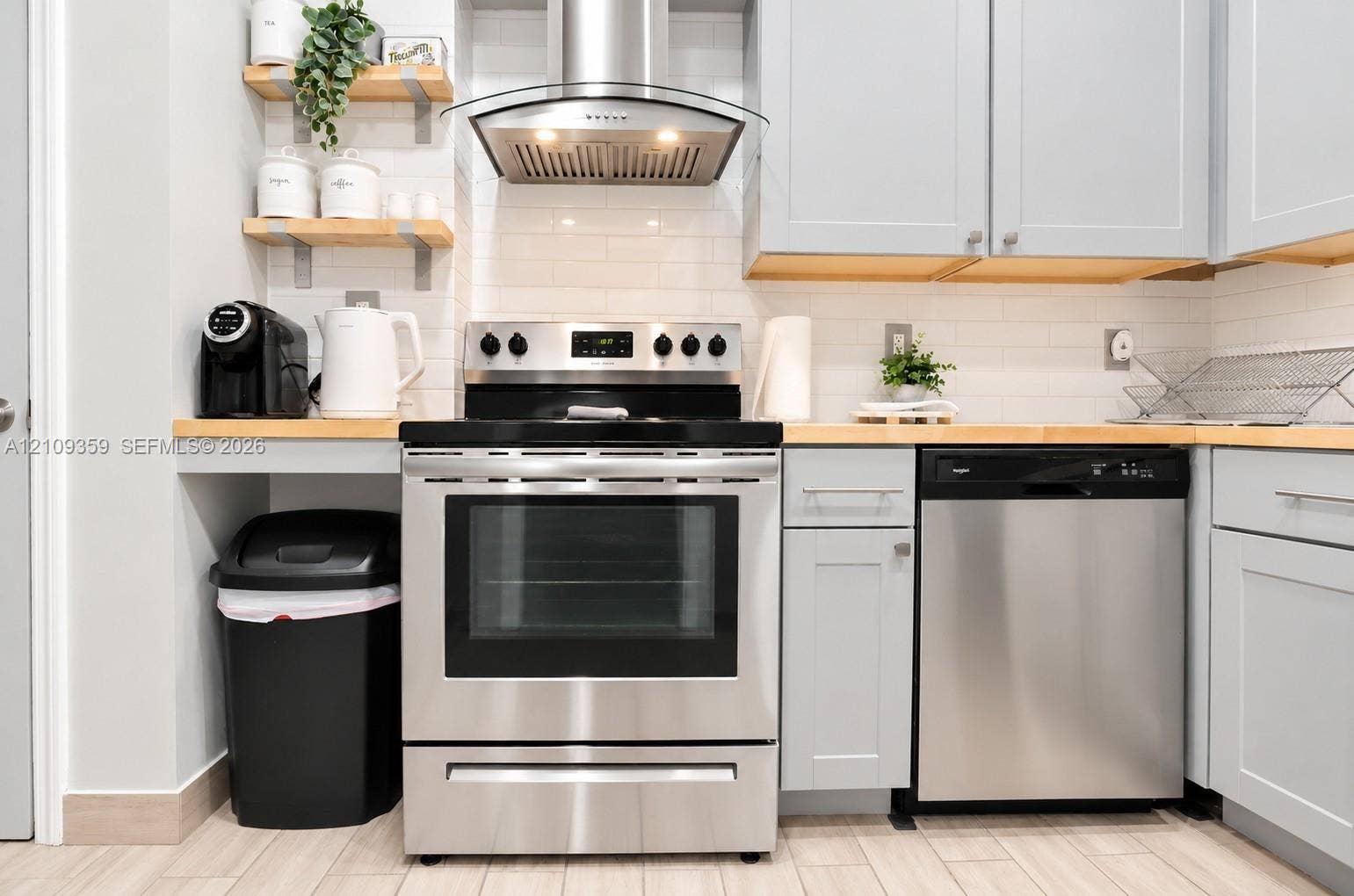 2426 SE 17th Causeway, #103A, Fort Lauderdale, FL 33316 Kitchen featuring light-toned cabinetry, wood countertops, stainless steel appliances, a subway tile backsplash, and wall-mounted shelving