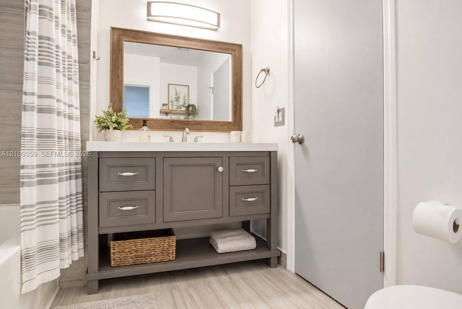 2426 SE 17th Causeway, #103A, Fort Lauderdale, FL 33316 Grey vanity featuring a white countertop, under-mount sink, integrated lower shelving, and a large wood-framed mirror with an overhead light fixture