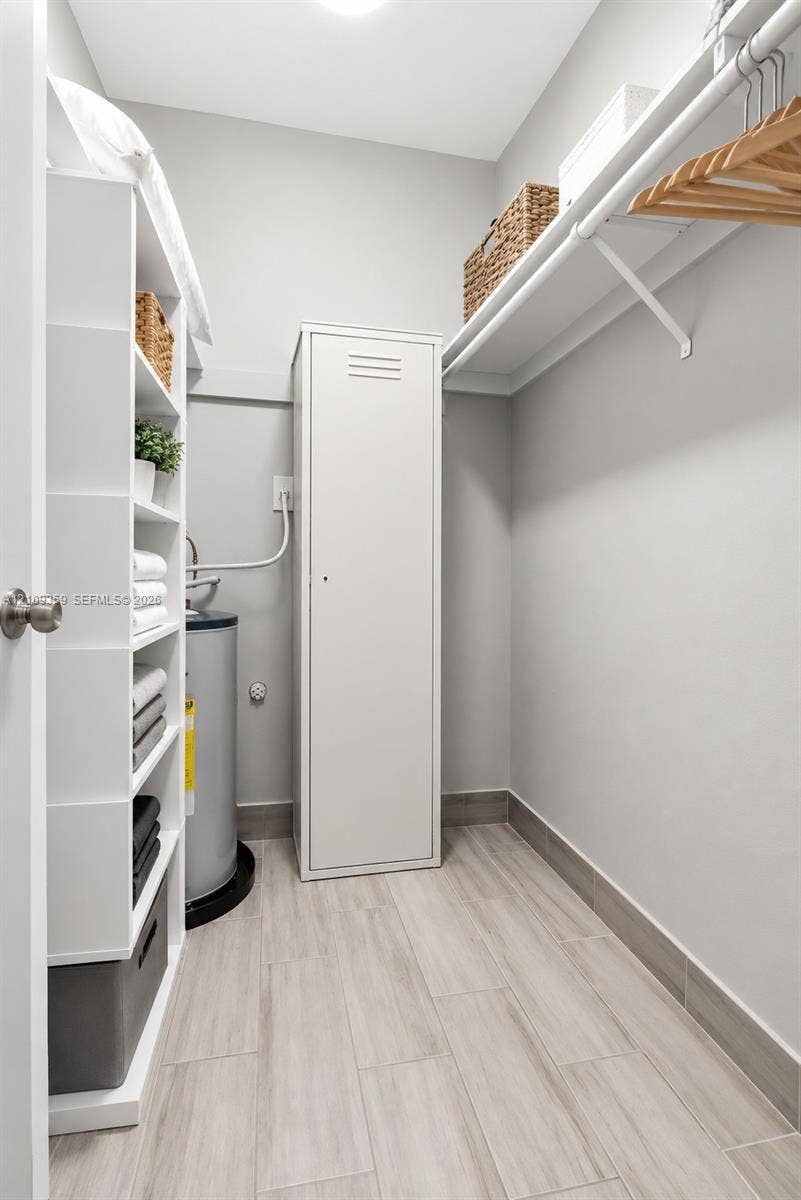 2426 SE 17th Causeway, #103A, Fort Lauderdale, FL 33316 Storage space featuring built-in white shelving, a full-height metal cabinet, wall-mounted hanging rod, and wood-finish tile flooring