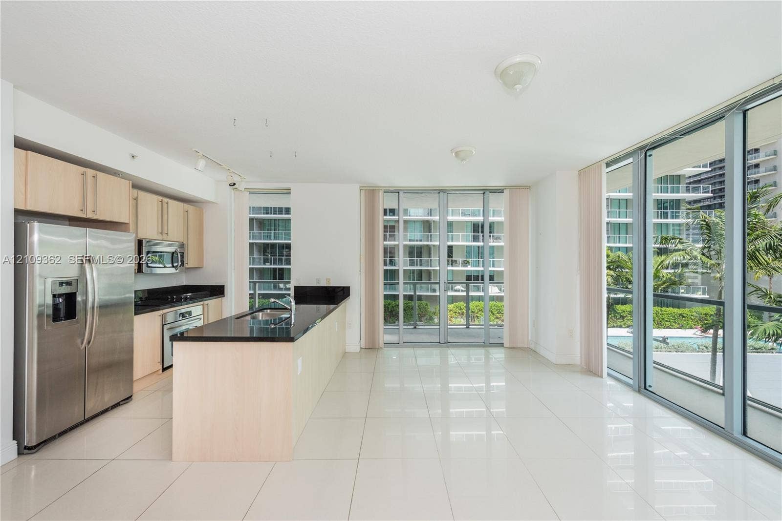 79 SW 12th Street, #1107-S, Miami, FL 33130 Kitchen area featuring light-finish cabinetry, dark solid-surface countertops, stainless steel appliances, floor-to-ceiling glass sliding doors, and light-toned tile flooring