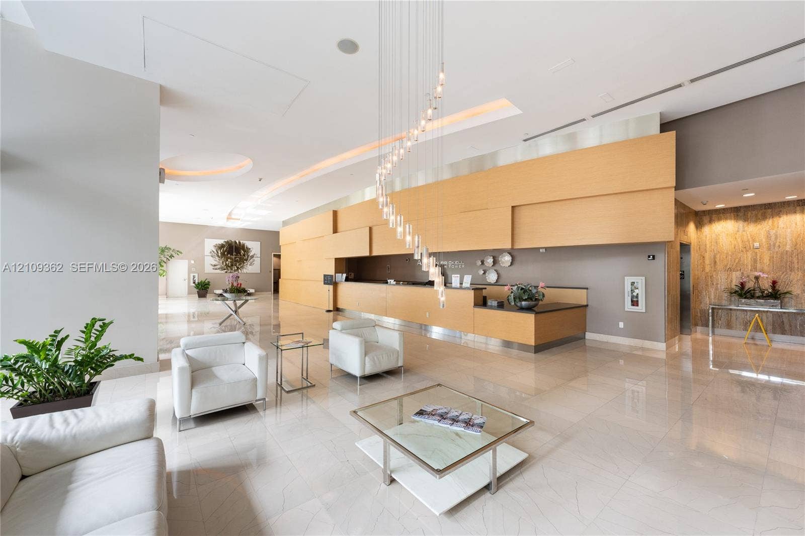 79 SW 12th Street, #1107-S, Miami, FL 33130 Spacious lobby featuring polished stone flooring, a multi-tiered spiral crystal chandelier, built-in reception desk with wood paneling, recessed lighting, and a textured stone feature wall