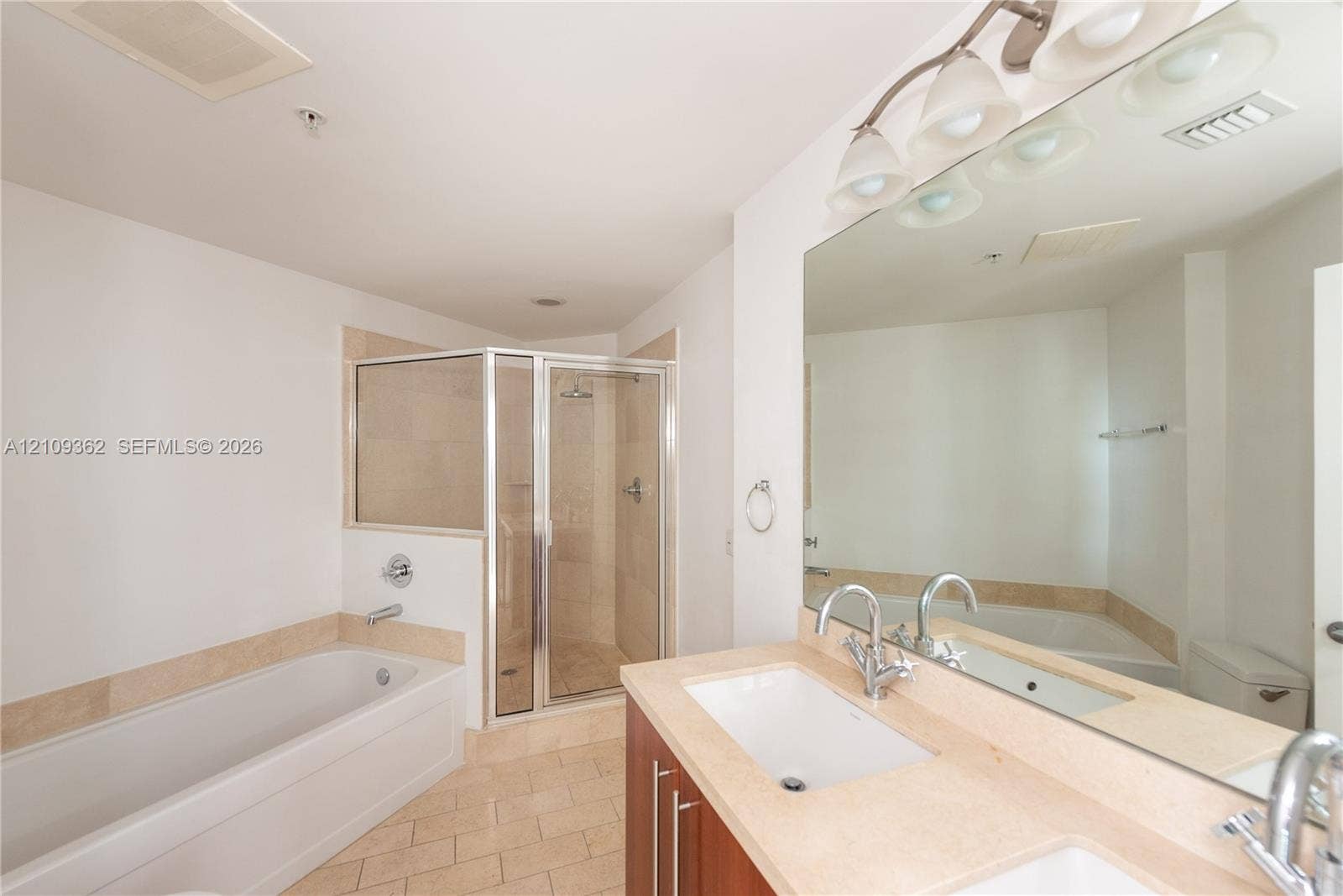 79 SW 12th Street, #1107-S, Miami, FL 33130 Bathroom featuring a wood-finish double vanity with a light-tone countertop, an expansive wall-to-wall mirror, a soaking tub with tile surround, and a glass-enclosed shower with tile wall finish