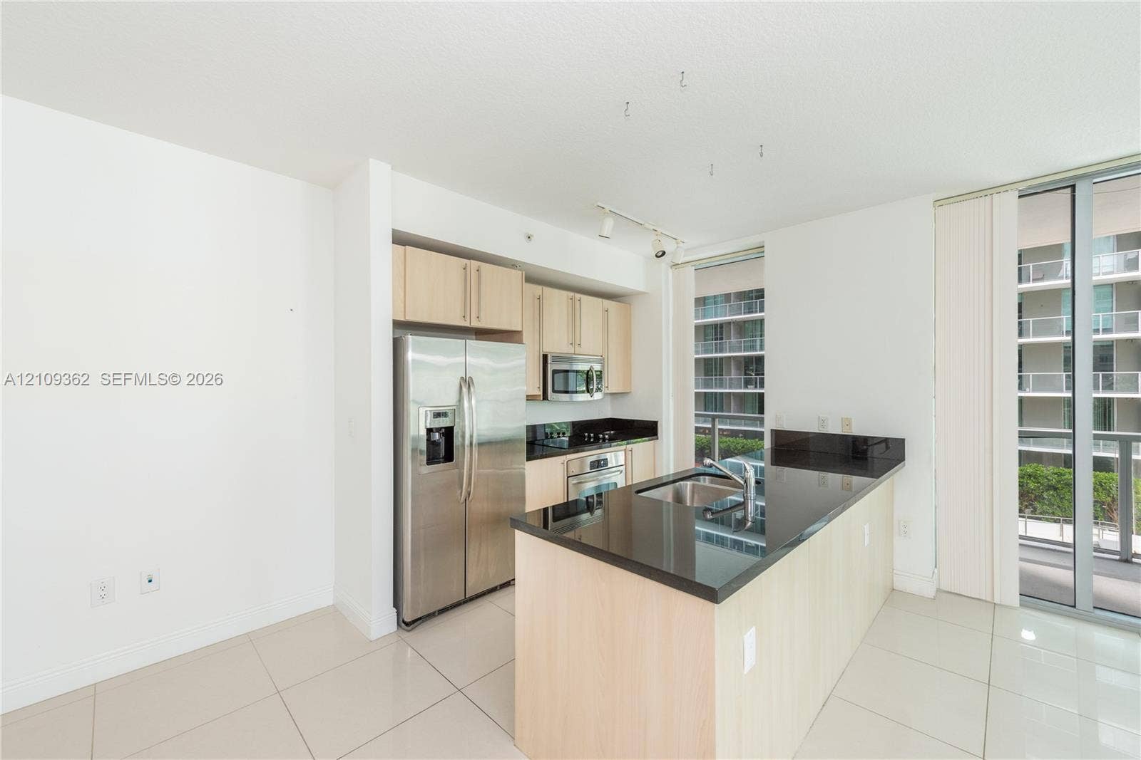 79 SW 12th Street, #1107-S, Miami, FL 33130 Kitchen featuring light wood-finish cabinetry, dark solid-surface countertops, stainless steel refrigerator, built-in microwave, and large-format tile flooring