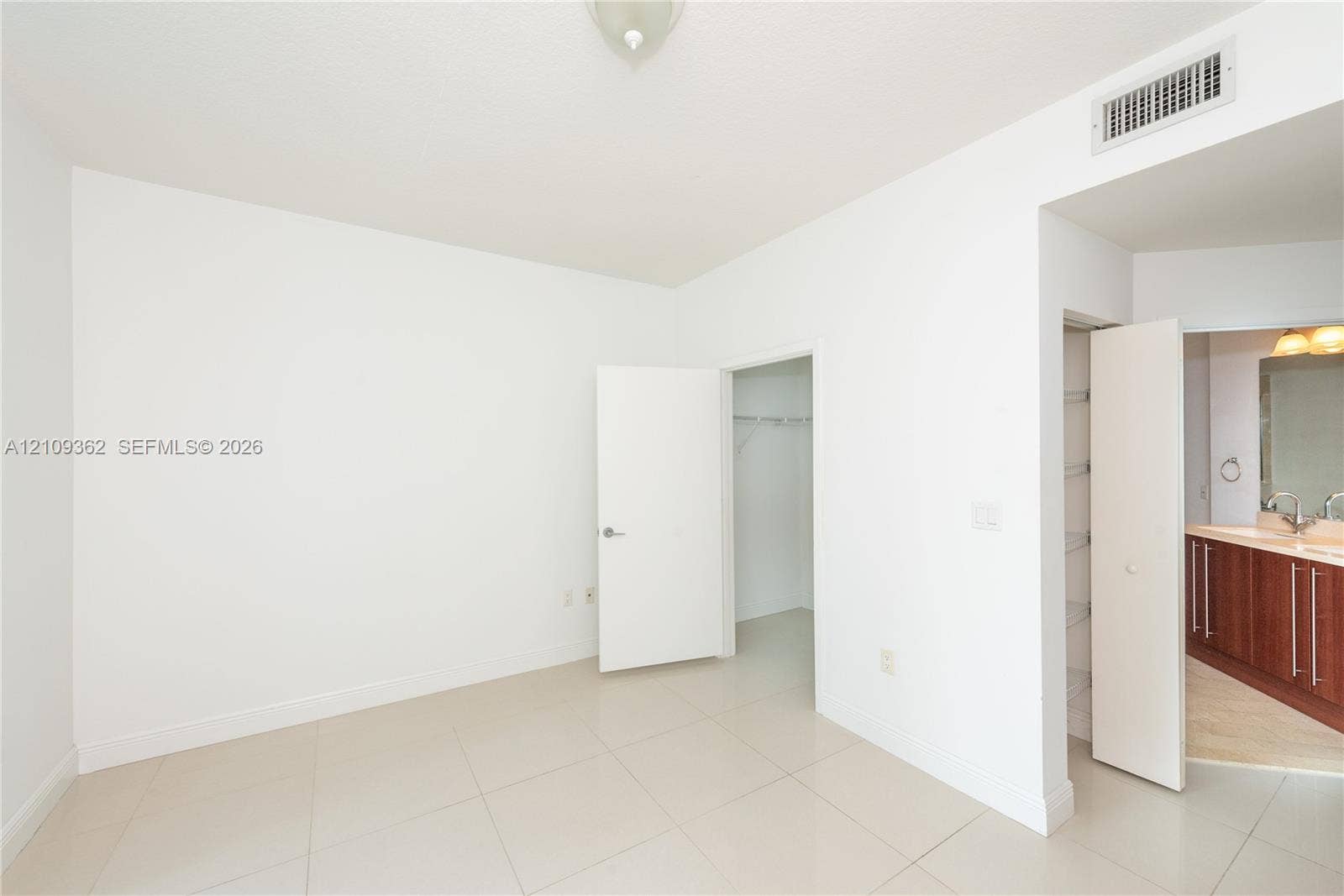 79 SW 12th Street, #1107-S, Miami, FL 33130 Neutral-toned tile flooring, walk-in closet with wire shelving, linen closet, and a bathroom featuring dark wood-finish cabinetry and a wide vanity mirror