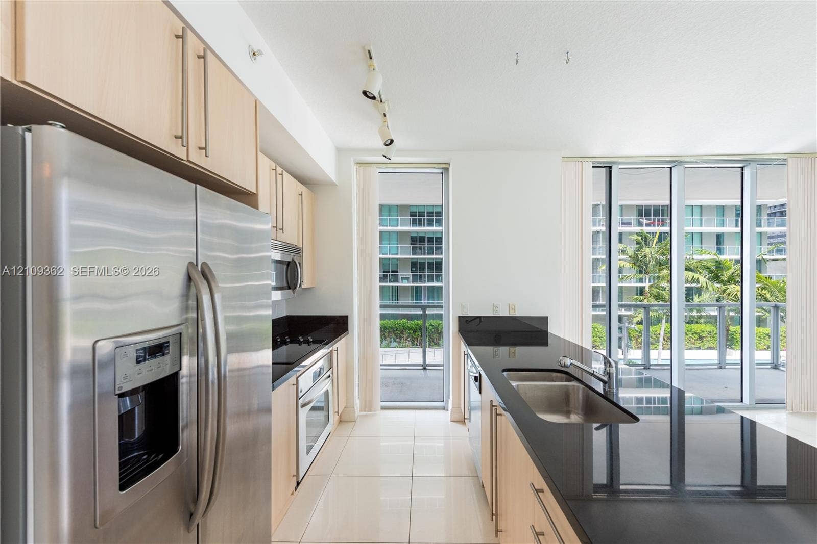79 SW 12th Street, #1107-S, Miami, FL 33130 Kitchen featuring light wood-finish cabinetry, black stone countertops, stainless steel appliances, tile flooring, and floor-to-ceiling windows