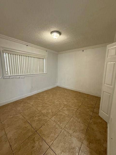 Room featuring neutral-toned tile flooring, crown molding, a flush-mount ceiling light fixture, and horizontal window blinds