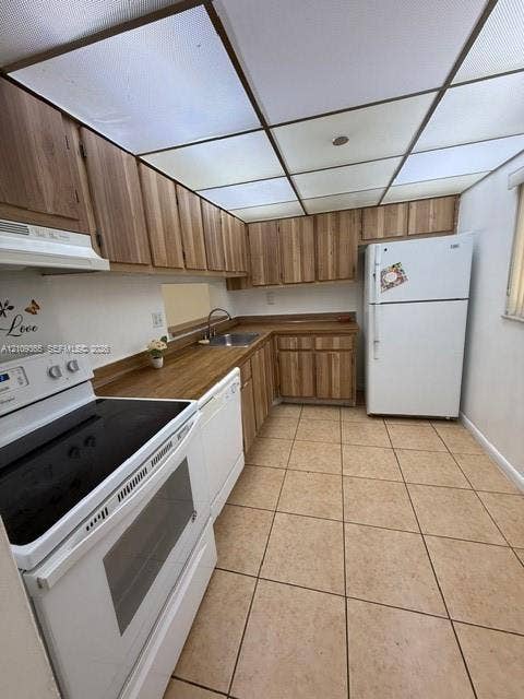 Kitchen featuring wood-finish cabinetry, solid surface countertops, ceramic tile flooring, and a dropped ceiling with integrated panel lighting