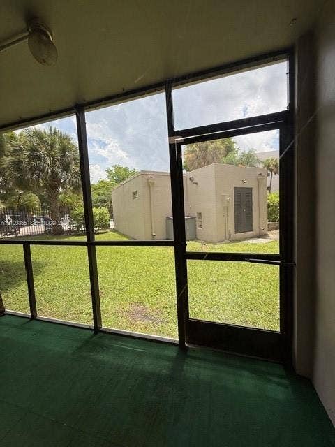 Screened-in enclosure featuring a metal-framed door, overhead light fixture, and green flooring