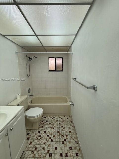 Bathroom featuring a drop-in bathtub with a wall-mounted showerhead, white tile tub surround, patterned mosaic floor tile, and a built-in white vanity