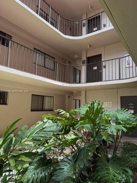 Exterior courtyard featuring multi-level walkways with metal railings, neutral-tone siding, and mature tropical greenery within a landscaped garden bed