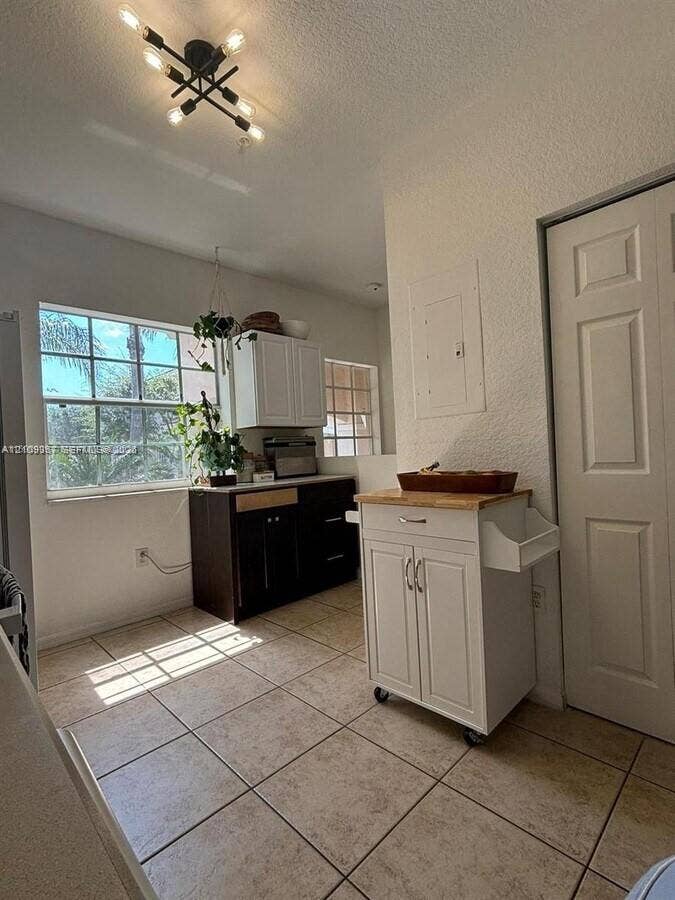 Multi-tone cabinetry featuring white upper cabinets and dark lower cabinetry, ceramic tile flooring, multi-pane window, and an industrial-style multi-arm ceiling light fixture