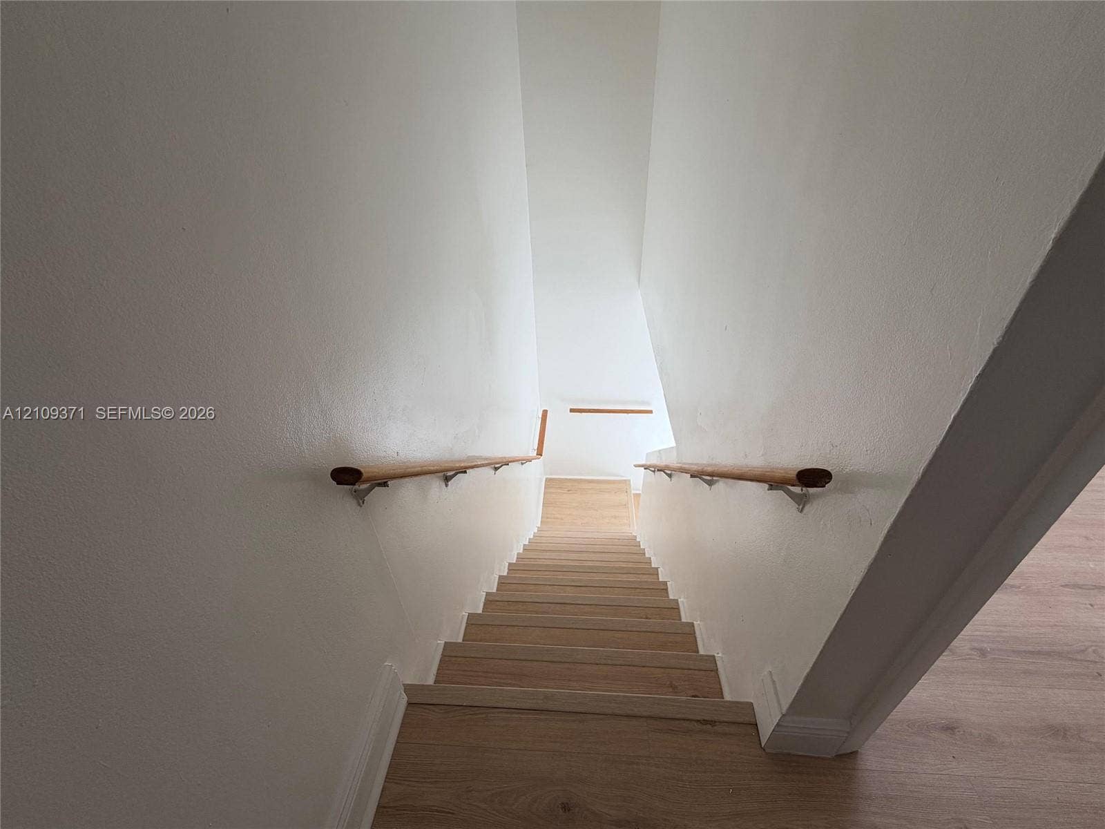 Staircase featuring wood-finish flooring and dual wooden handrails with metal brackets