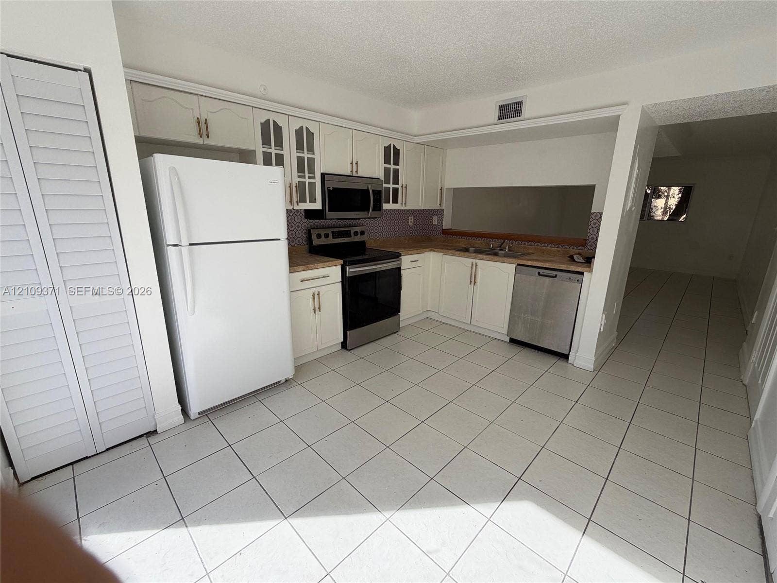 Kitchen featuring white cabinetry with glass-panel upper doors, stainless steel appliances, patterned backsplash, and tile flooring