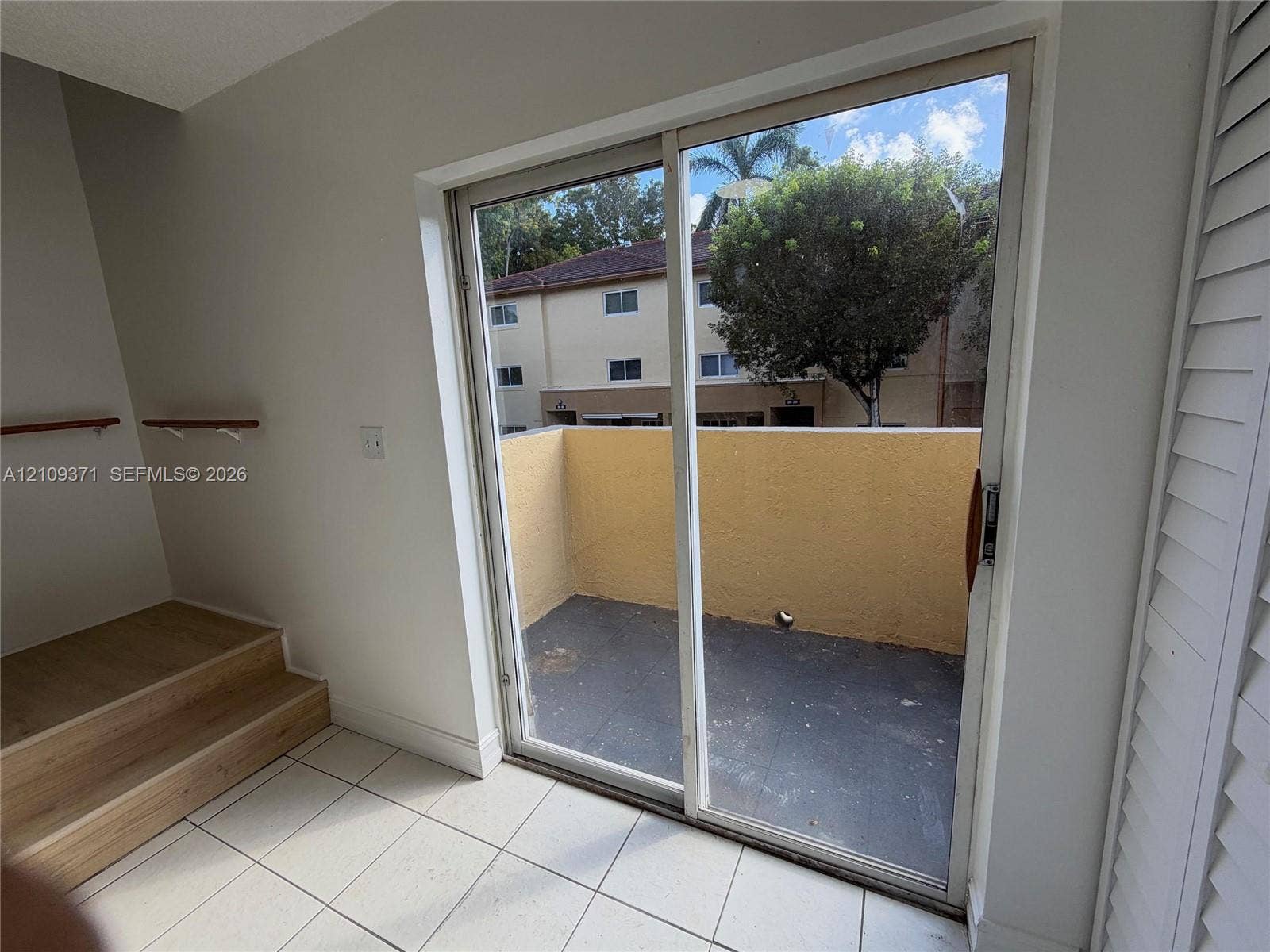 Sliding glass door opening to a private balcony with stucco surround, complemented by tile flooring and an elevated wood-finish platform