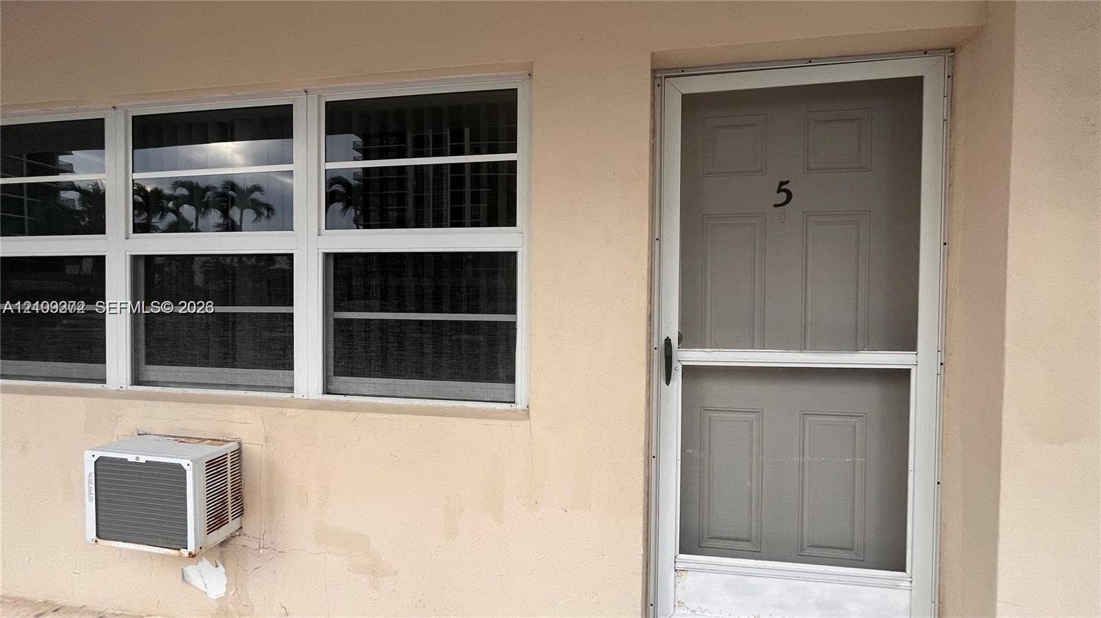 Exterior entrance featuring a white-framed storm door, grid-patterned windows, and a dedicated wall-mounted air conditioning unit