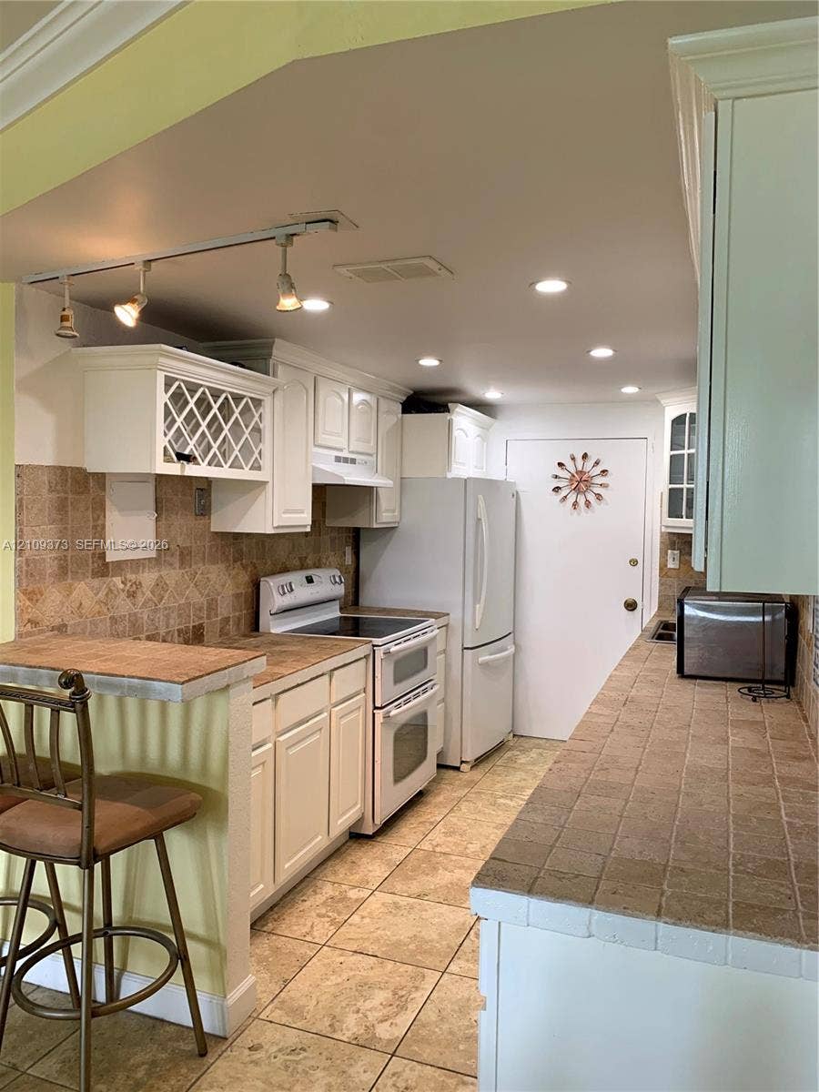 Kitchen featuring white cabinetry with lattice detail, tiled countertops, tile backsplash, tile flooring, and track lighting