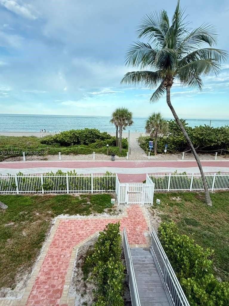 Private walkway featuring red brick pavers, a white picket fence with gated access, and mature palm trees