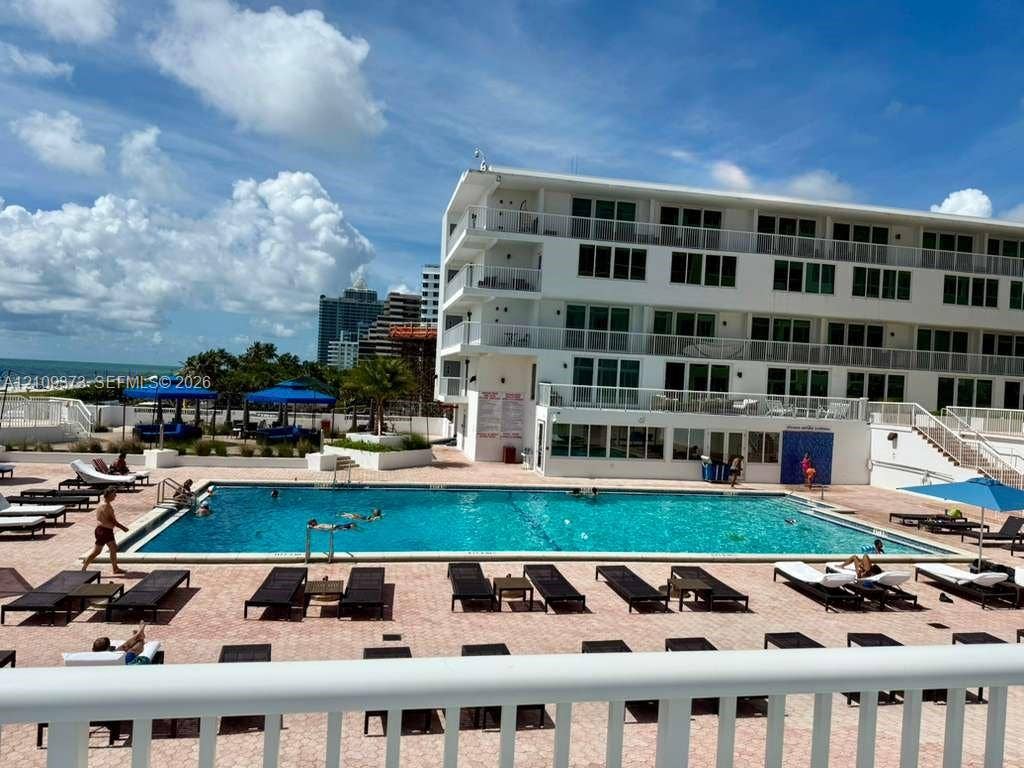 Multi-story residential building featuring a rectangular swimming pool, expansive paved pool deck, and private balcony railings