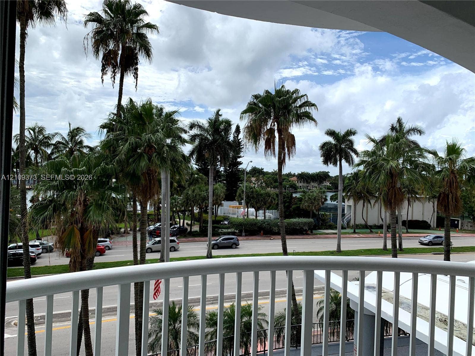 Covered balcony featuring white vertical railings and mature palm trees