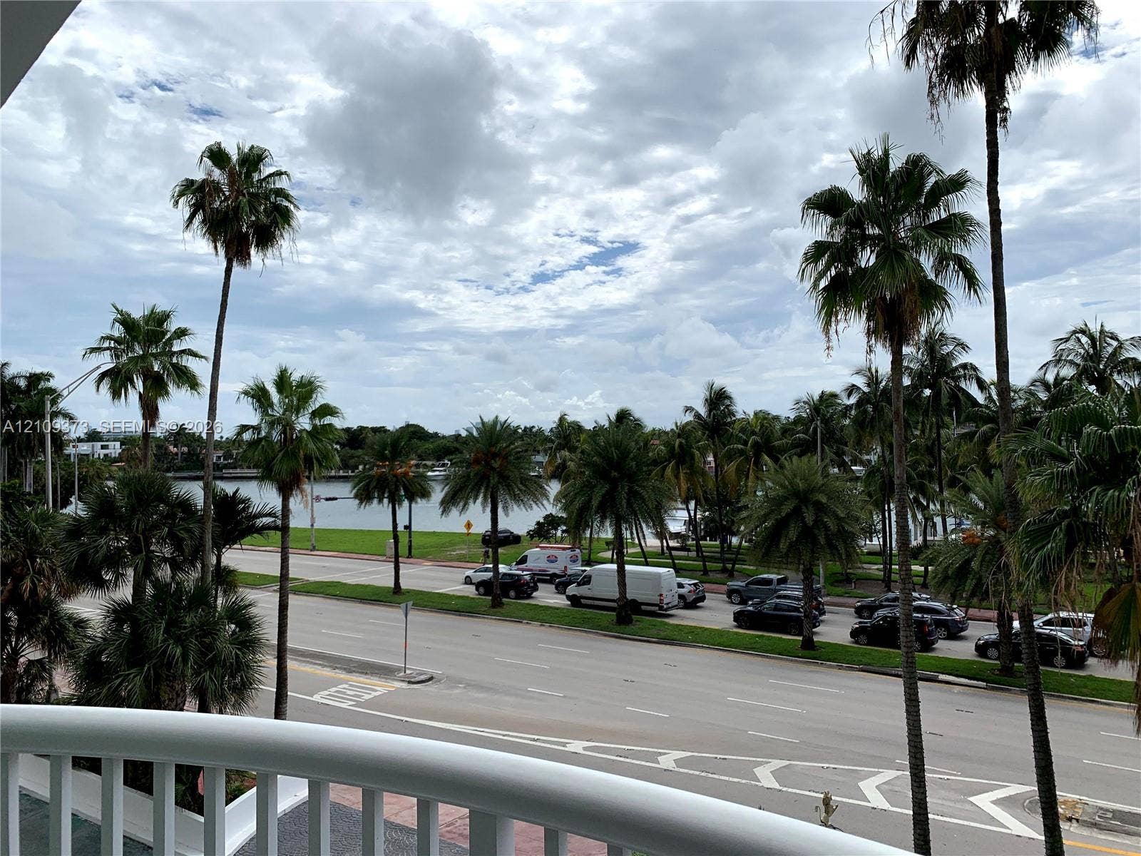 Exterior balcony featuring a white railing and a backdrop of mature palm trees overlooking a waterway
