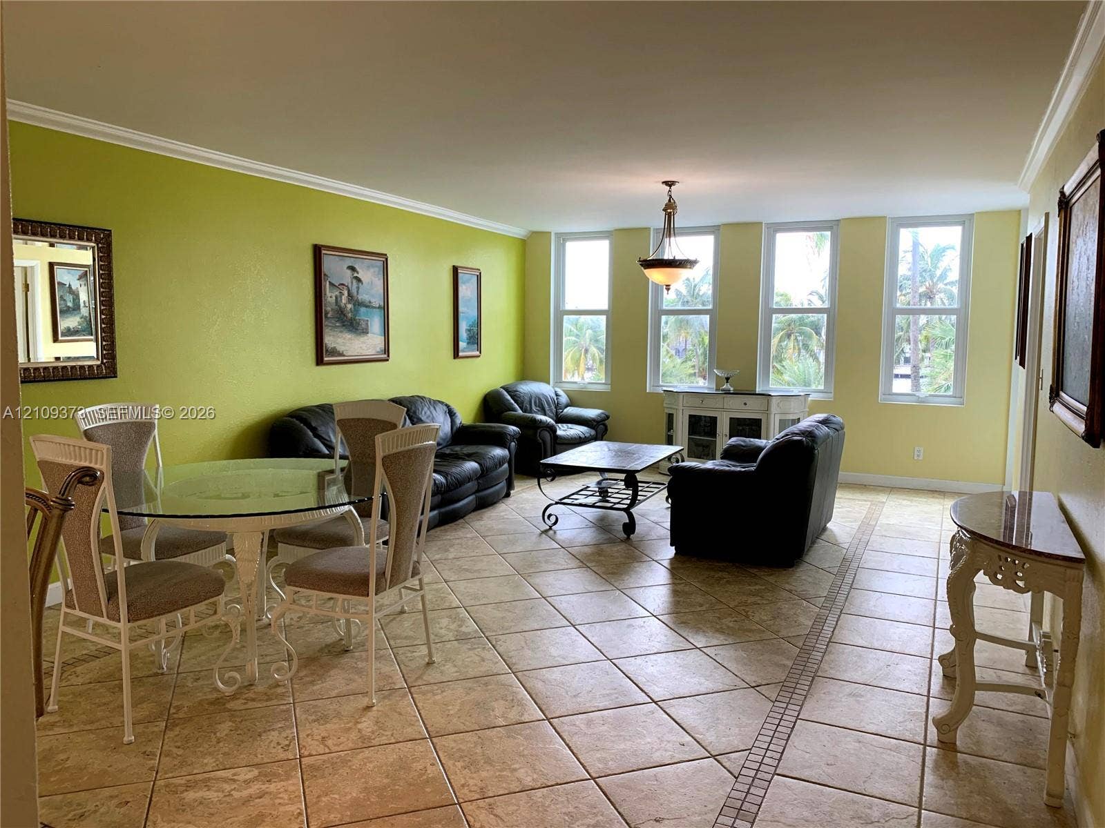 Open-concept living space featuring large-format diagonal tile flooring, multi-panel windows, crown molding, and a decorative pendant light fixture