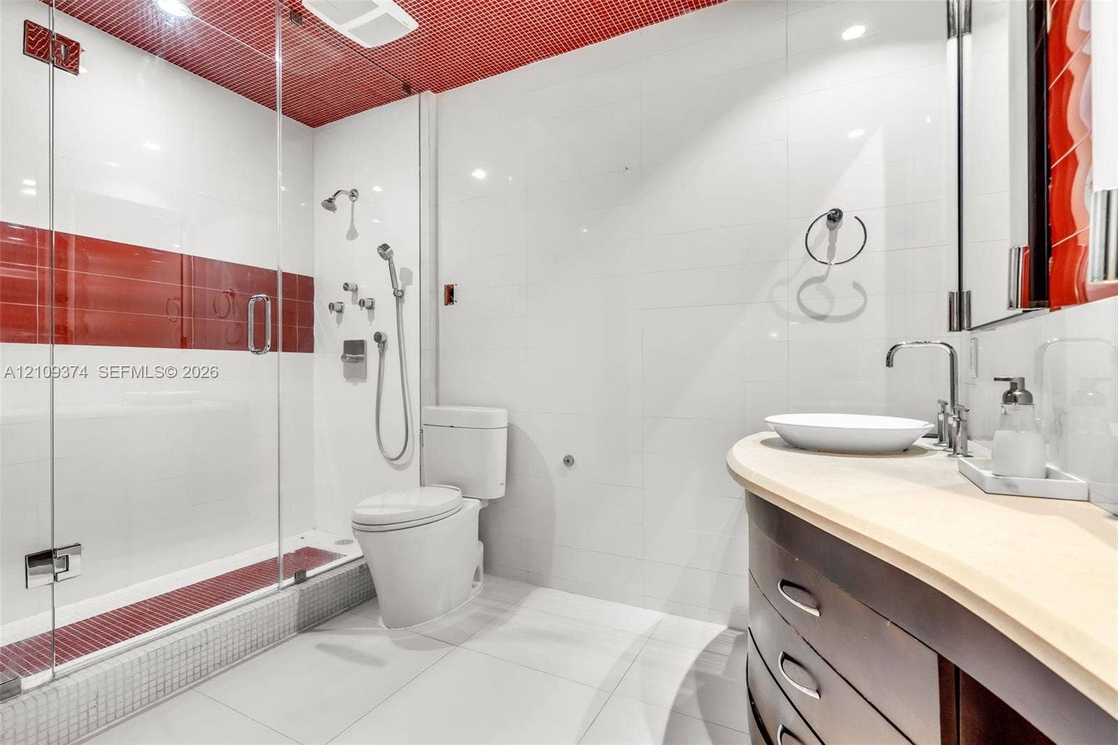 100 N Federal Highway, #1, Fort Lauderdale, FL 33301 Bathroom featuring a glass-enclosed shower with multi-head fixtures and decorative tile accents, a curved wood-finish vanity with a vessel sink, and a high-profile toilet