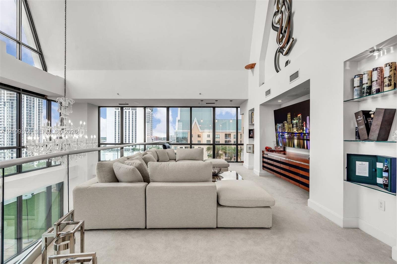 100 N Federal Highway, #1, Fort Lauderdale, FL 33301 Vaulted ceilings with floor-to-ceiling windows, crystal chandelier, built-in horizontal wood-slat cabinetry, and integrated glass shelving
