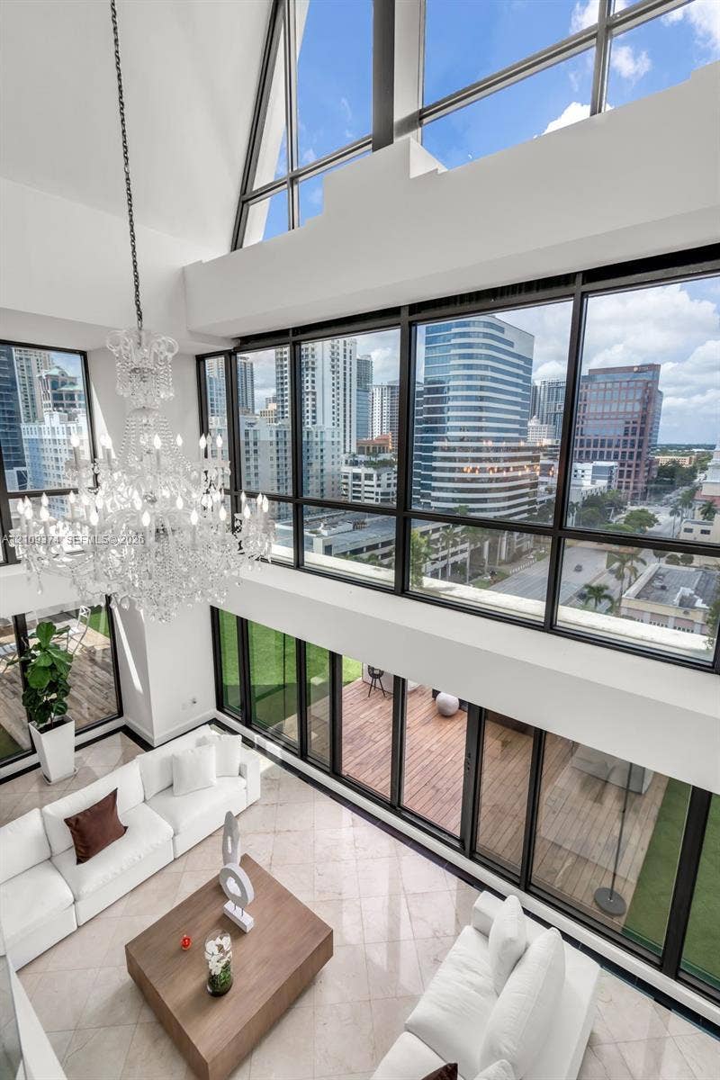 100 N Federal Highway, #1, Fort Lauderdale, FL 33301 Double-height vaulted ceilings featuring floor-to-ceiling multi-story windows, polished stone flooring, intricate tiered crystal chandelier, and direct access to a wood-decked outdoor terrace