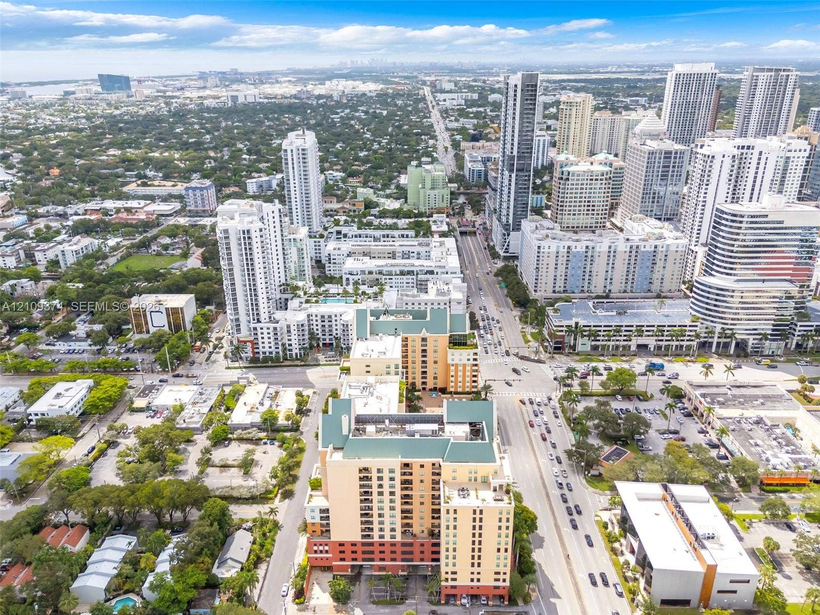 100 N Federal Highway, #1, Fort Lauderdale, FL 33301 Aerial perspective of a multi-story urban complex featuring a prominent peaked roofline, stucco-finish facade, ground-level parking access, and extensive perimeter greenery