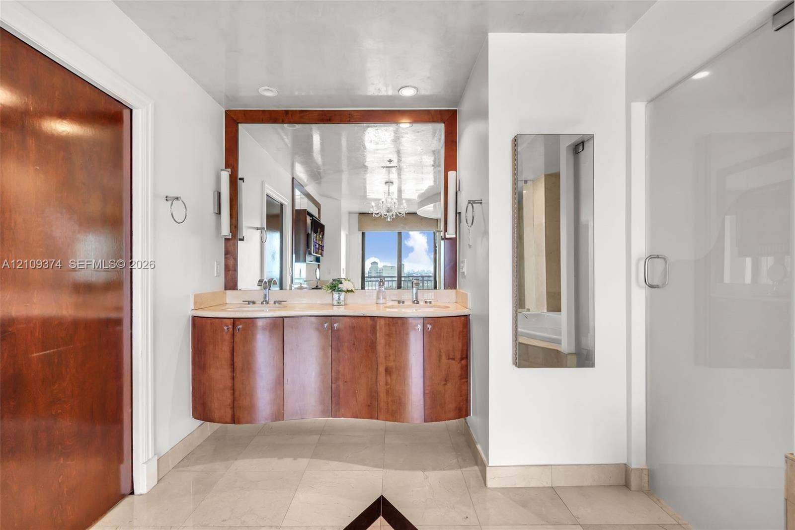 100 N Federal Highway, #1, Fort Lauderdale, FL 33301 Floating curved wood-finish vanity with dual integrated sinks, stone-surface countertop, full-width mirror, and glass-enclosed shower