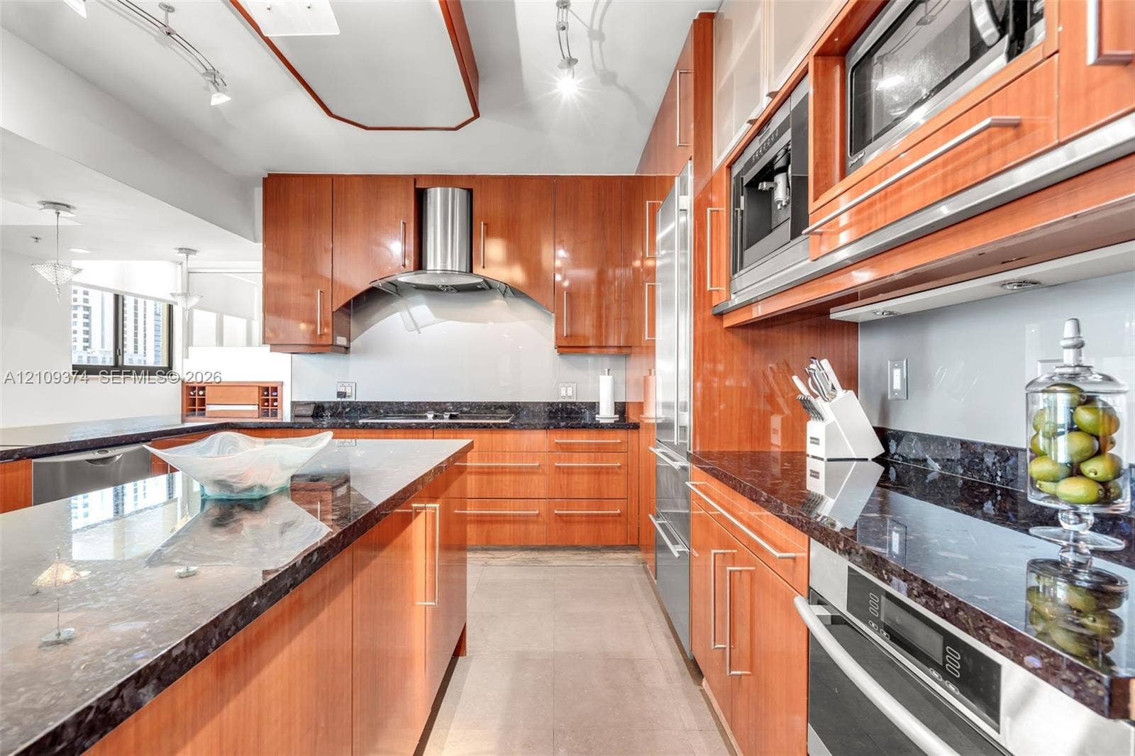100 N Federal Highway, #1, Fort Lauderdale, FL 33301 Kitchen featuring warm-toned cabinetry, expansive stone countertops, built-in stainless steel appliances, a professional-style range hood, and track lighting
