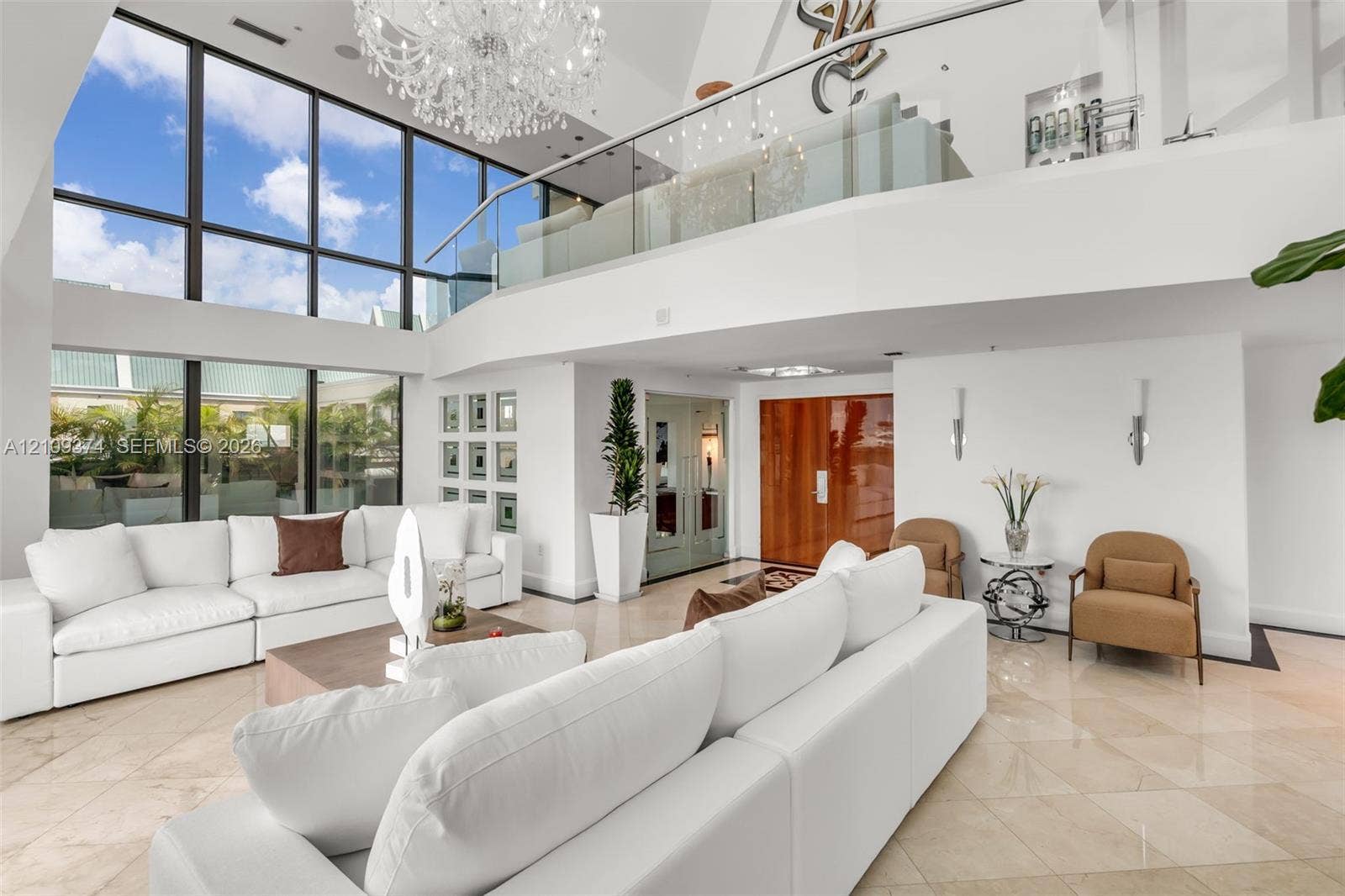 100 N Federal Highway, #1, Fort Lauderdale, FL 33301 Double-height living area featuring floor-to-ceiling windows, polished stone flooring, a glass mezzanine railing, and a grand crystal chandelier