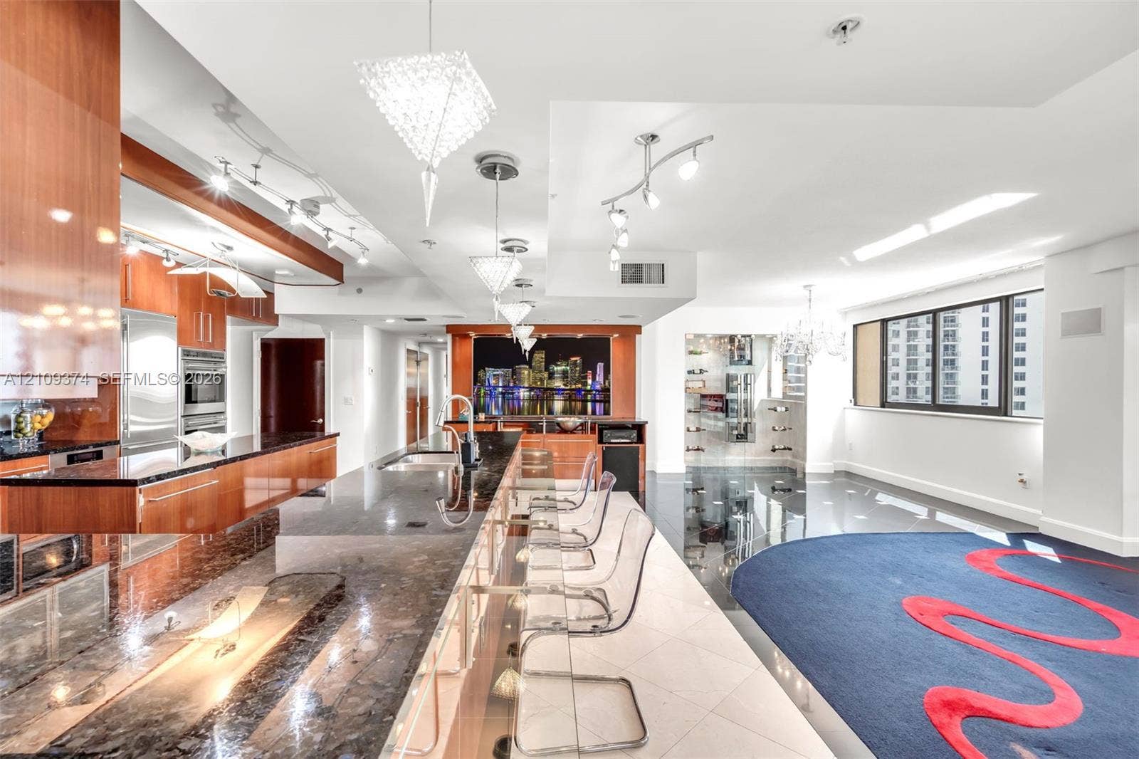 100 N Federal Highway, #1, Fort Lauderdale, FL 33301 Contemporary kitchen featuring high-gloss wood-finish cabinetry, expansive stone countertops, integrated stainless steel appliances, a tiered island with built-in seating, and intricate custom overhead lighting