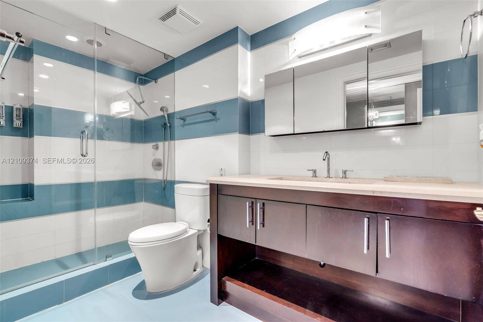 100 N Federal Highway, #1, Fort Lauderdale, FL 33301 Bathroom featuring a glass-enclosed shower, wood-finish vanity with stone countertop, integrated undermount sink, and multi-tone horizontal wall tiling