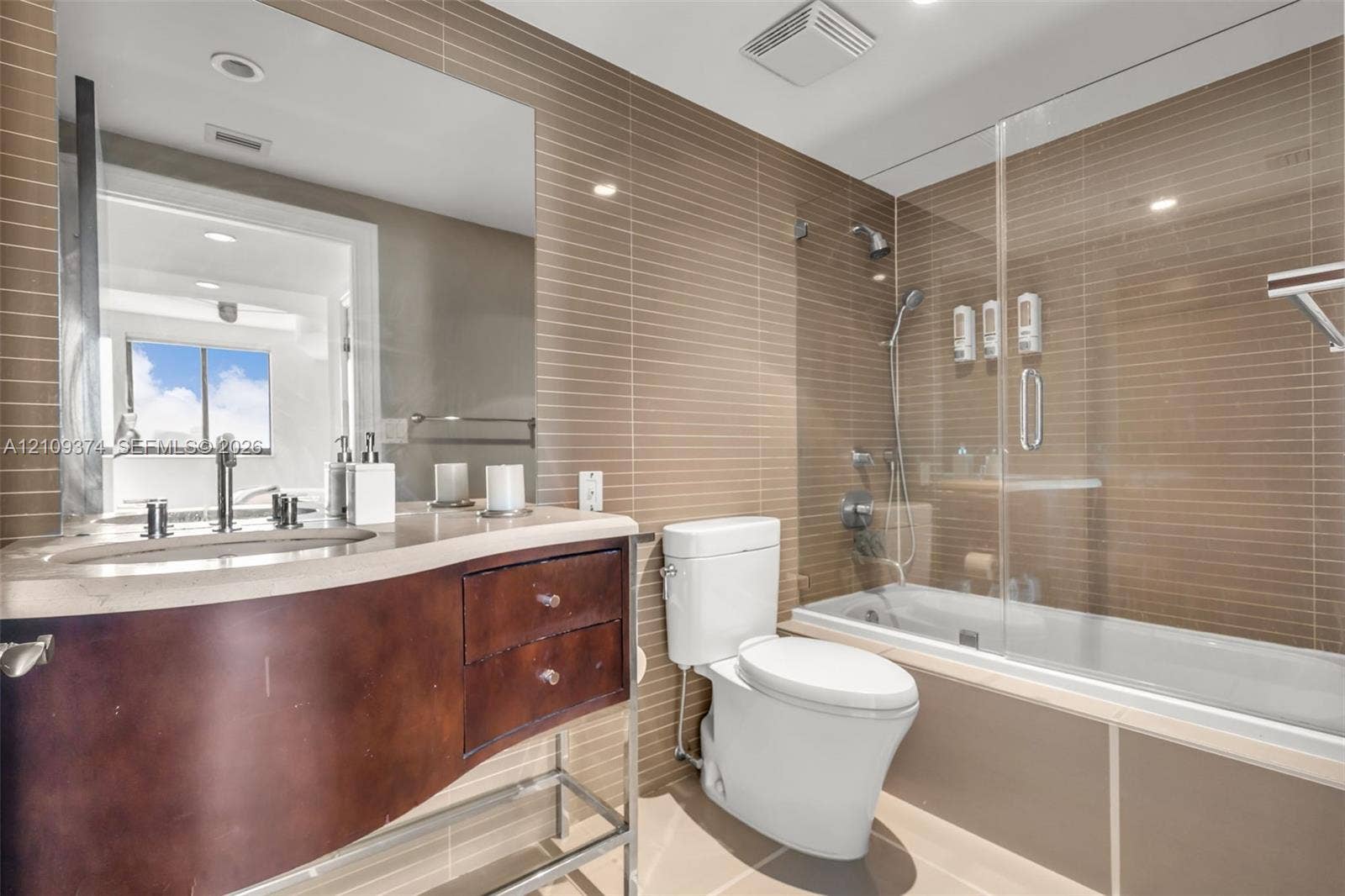 100 N Federal Highway, #1, Fort Lauderdale, FL 33301 Bathroom featuring a curved vanity with stone countertop, horizontal tile wall accents, and a glass-enclosed shower and tub combination