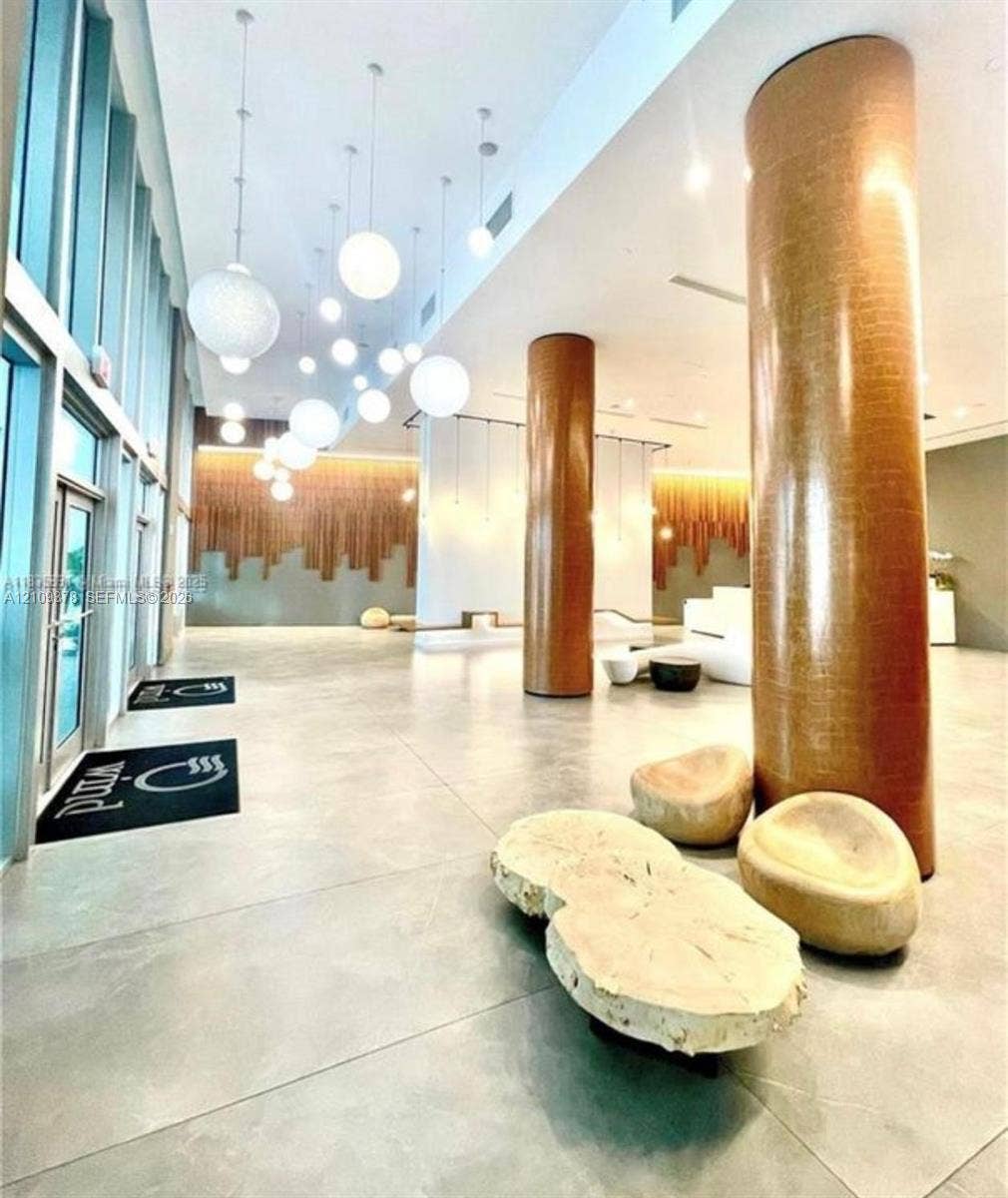 350 S Miami Avenue, #2207, Miami, Miami, FL 33130 Grand lobby entrance featuring high ceilings, floor-to-ceiling windows, polished stone flooring, custom pendant globe lighting, and textured metallic-finish structural columns