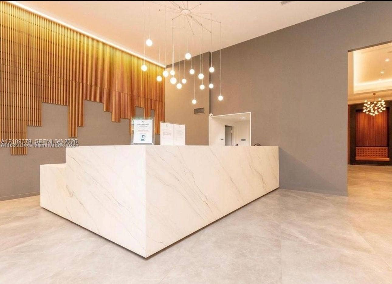 350 S Miami Avenue, #2207, Miami, Miami, FL 33130 Reception area featuring a stone-finish desk, vertical slat wood wall paneling, large-format tile flooring, and a multi-bulb pendant chandelier