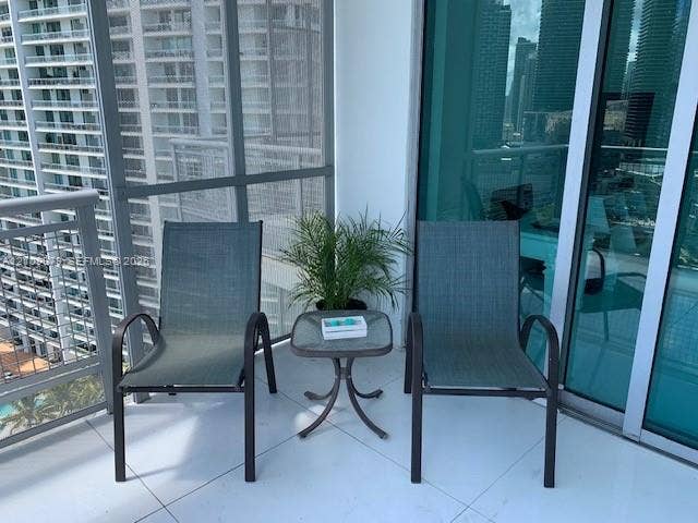 Covered balcony featuring white tile flooring, metal railings, and floor-to-ceiling glass paneling