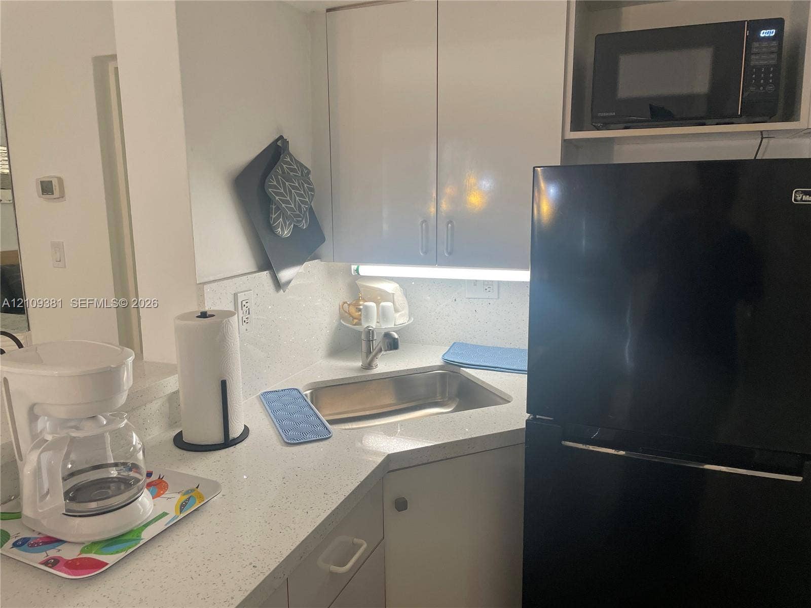 26 Diplomat Parkway, #2351, Hallandale Beach, FL 33009 Kitchen area featuring a quartz countertop peninsula, white cabinetry, a built-in microwave, a stainless steel sink, and light-toned tile flooring