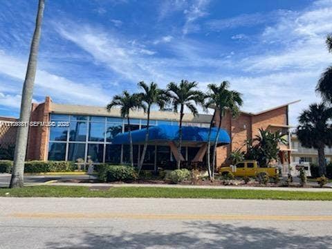 26 Diplomat Parkway, #2351, Hallandale Beach, FL 33009 Expansive glass-paneled facade featuring brick exterior elements and a prominent blue covered entryway