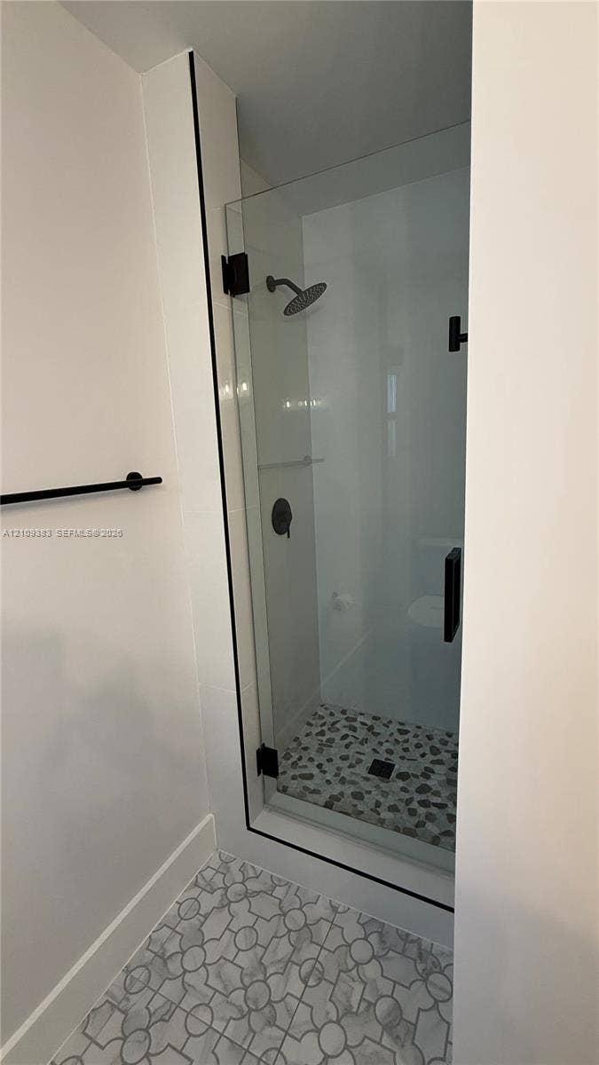 10751 SW 48th Street, Davie, Davie, FL 33328 Walk-in shower featuring a frameless glass door, matte black fixtures, pebble tile flooring, and geometric pattern floor tile