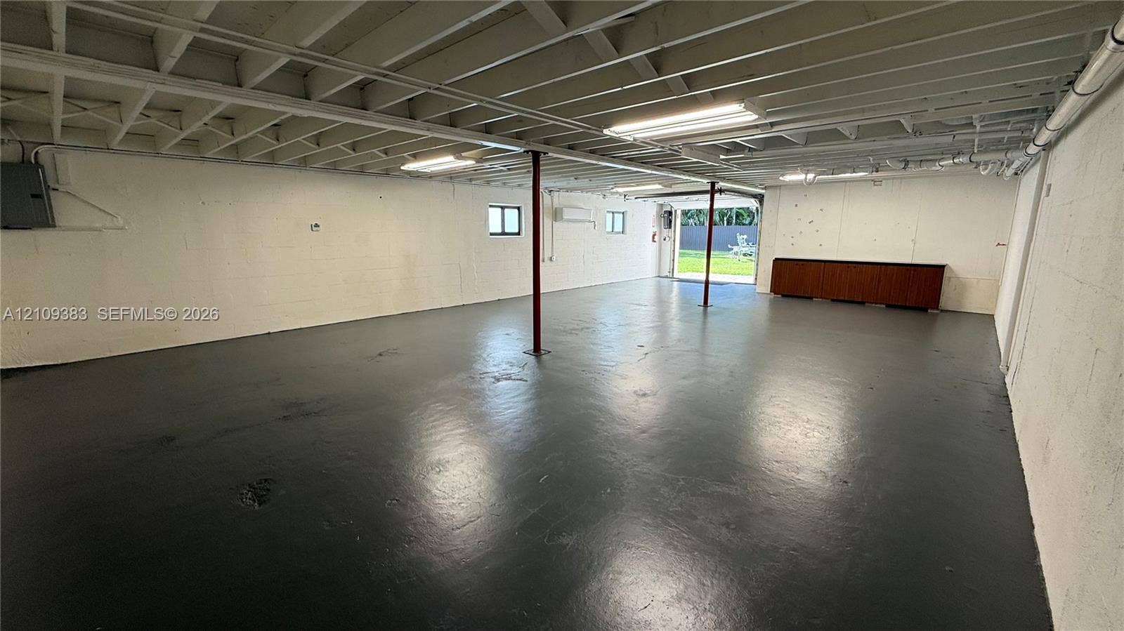 10751 SW 48th Street, Davie, Davie, FL 33328 Open-concept utility space featuring painted masonry walls, sealed concrete flooring, exposed ceiling joists, linear fluorescent lighting, and built-in cabinetry