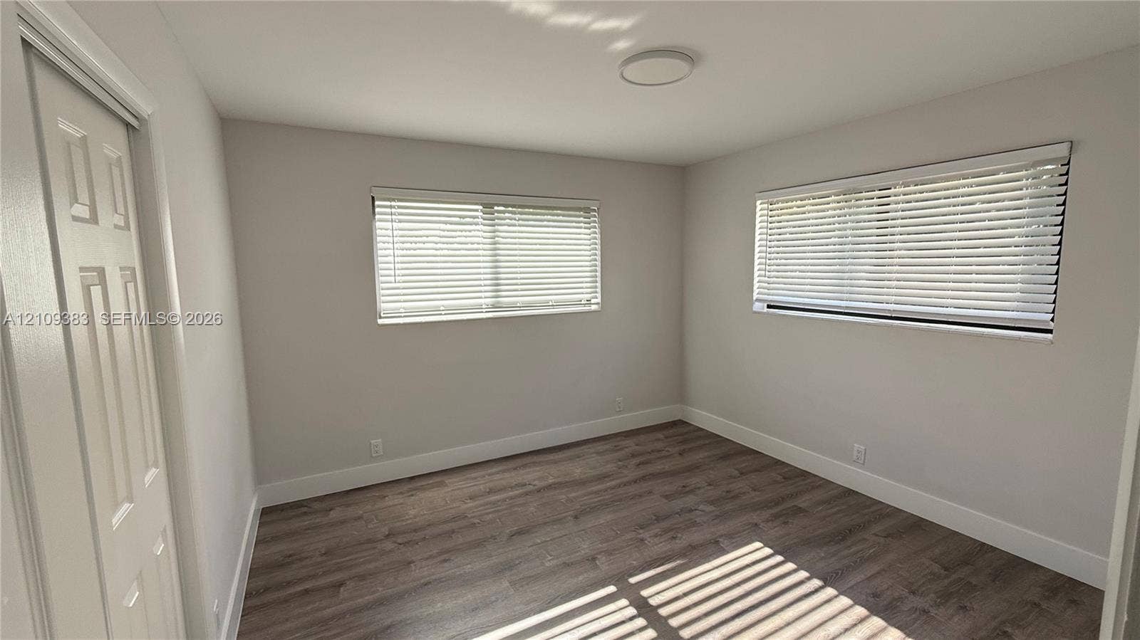 10751 SW 48th Street, Davie, Davie, FL 33328 Wood-finish flooring, neutral wall tones, two windows with horizontal blinds, and a flush-mount overhead light fixture